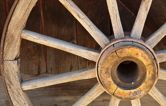 wagon wheel leans against rough side of barn