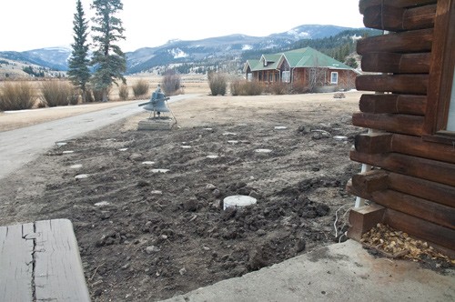 view from lodge porch of area where new deck will be. Concrete footers are buried in uncovered earth