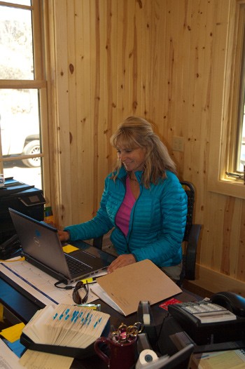 blonde woman with blue jacket smiles at computer at colorado fly fishing guest ranch