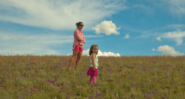 mother and daughter stand on flower covered mountainside with bright blue sky in background