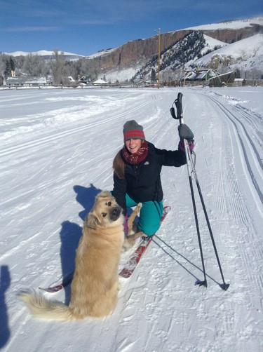 woman squats to pet dog during her ski. Both look toward camera