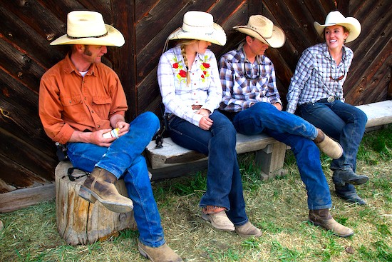 Four wranglers sitting on a bench outside the barn talking