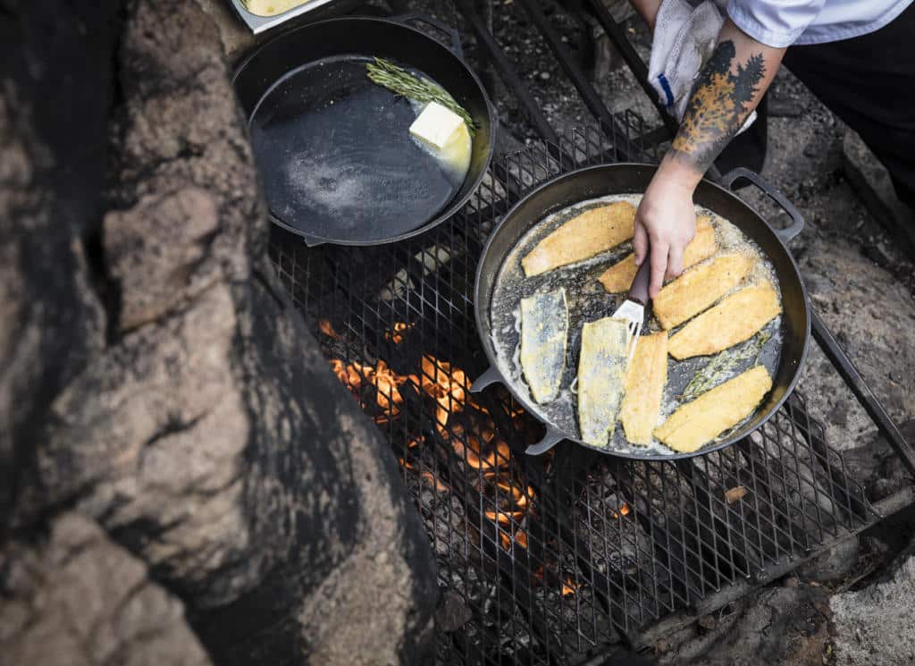 breaded trout is cooked in a large, cast iron skillet, over a campfire.
