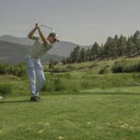 A golfer mid swing on a par 3 tee box