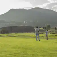 Two golfers stand in the fairway as one hits their ball towards the green