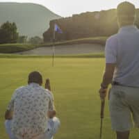 Two golfers stand on the green at sunset reading their putts