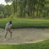 A golfer sets up in a sand bunker next to the green