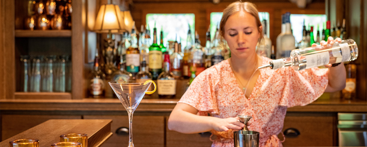 A female bartender makes a martini at an oak bar